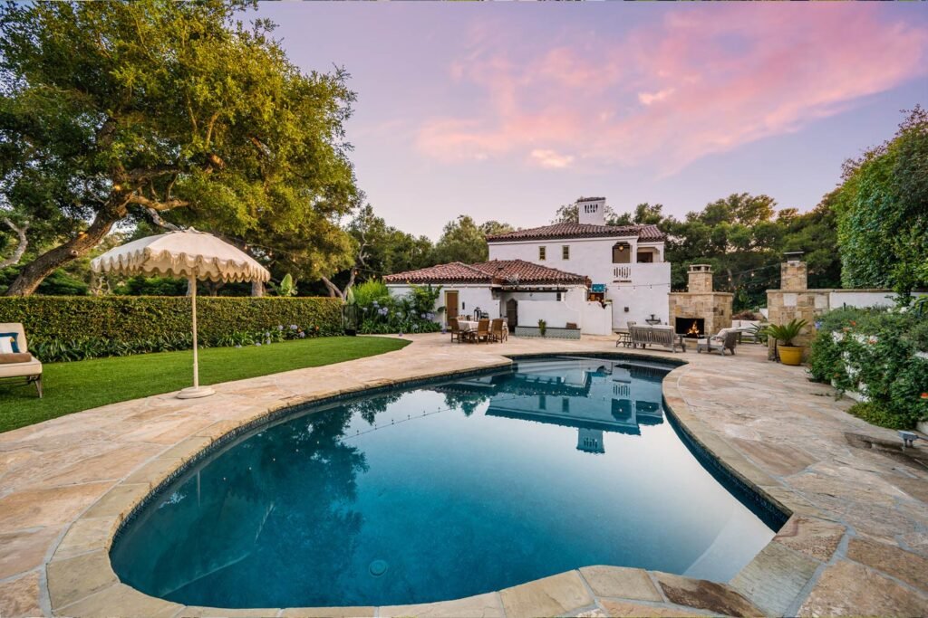 alberca en un atardecer, sombrilla y area para relajarse. al fondo casa blanca
